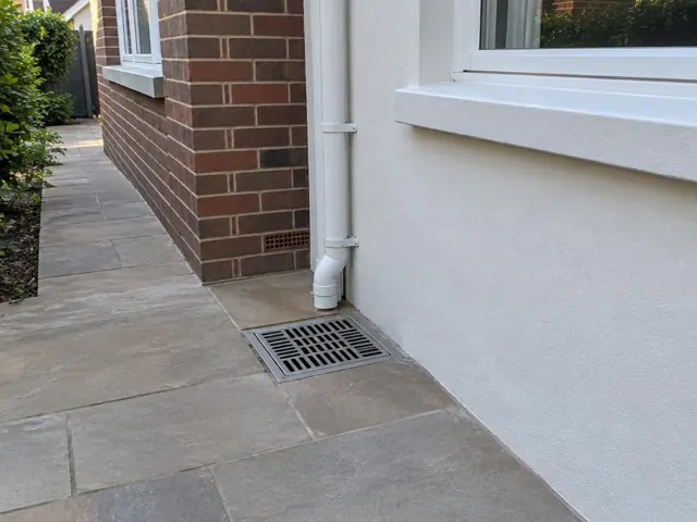 Outdoor gully grate seated beside brick and rendered wall on dry paved side passage in Willoughby
